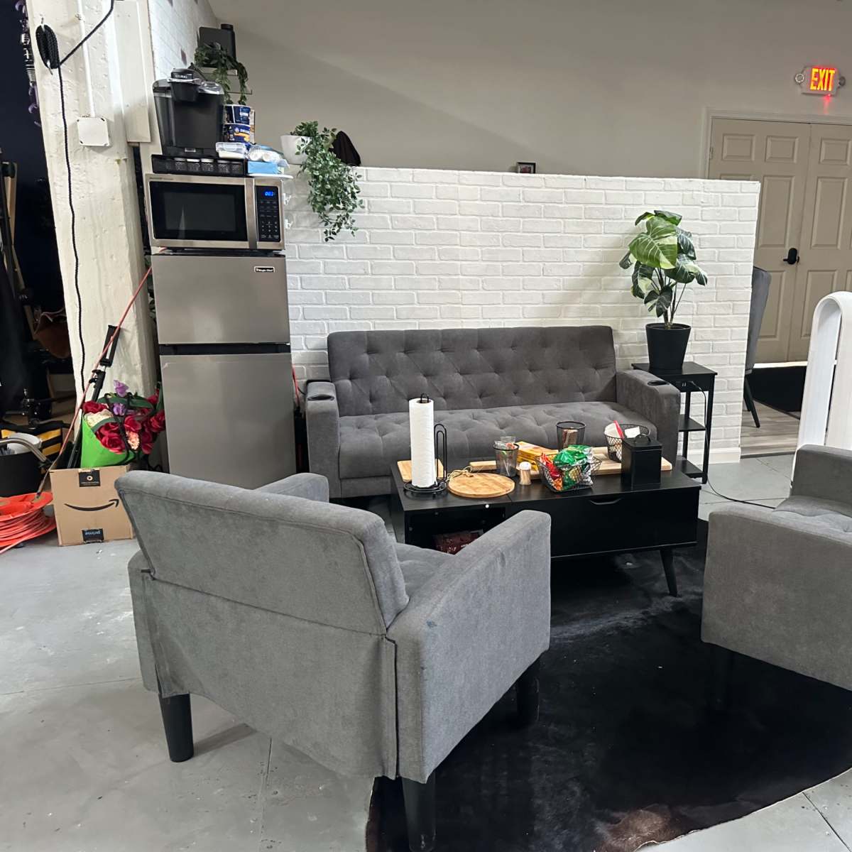 A cozy seating area with a gray sofa and two armchairs arranged around a black coffee table in front of a white brick wall.