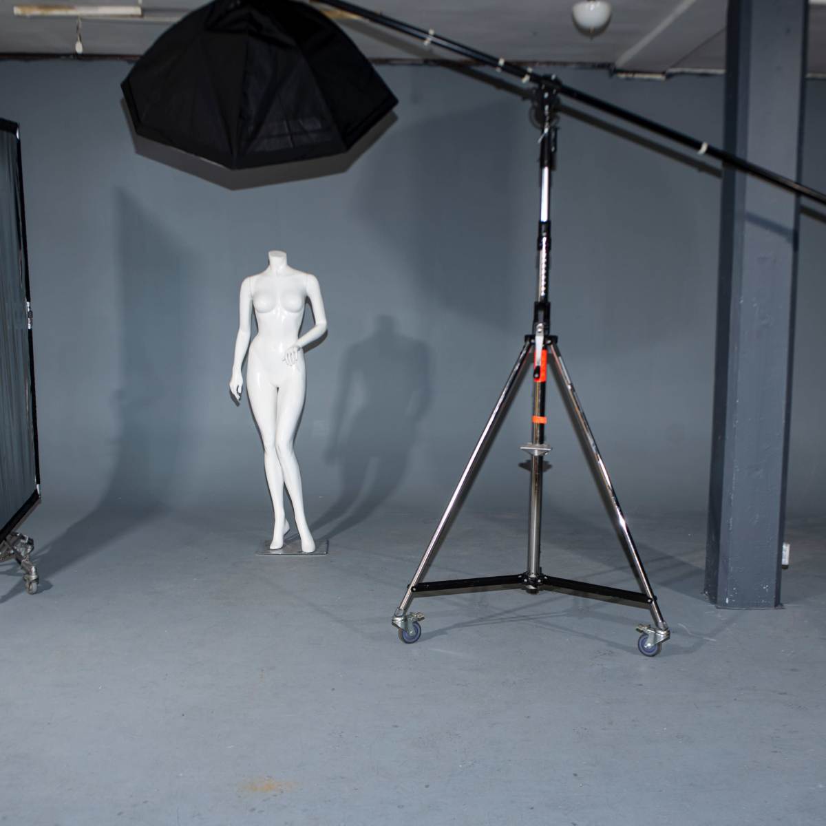 A photography studio setup with a mannequin, a large light modifier on a stand, and a black backdrop.