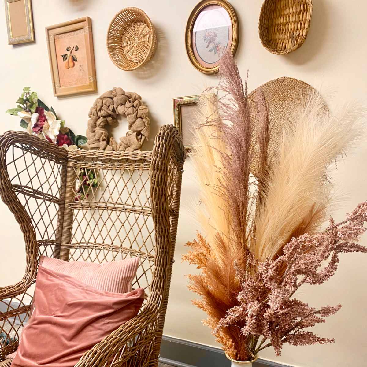A wicker chair is positioned next to a vase filled with dried flowers, set against a wall adorned with various framed artworks and woven baskets.