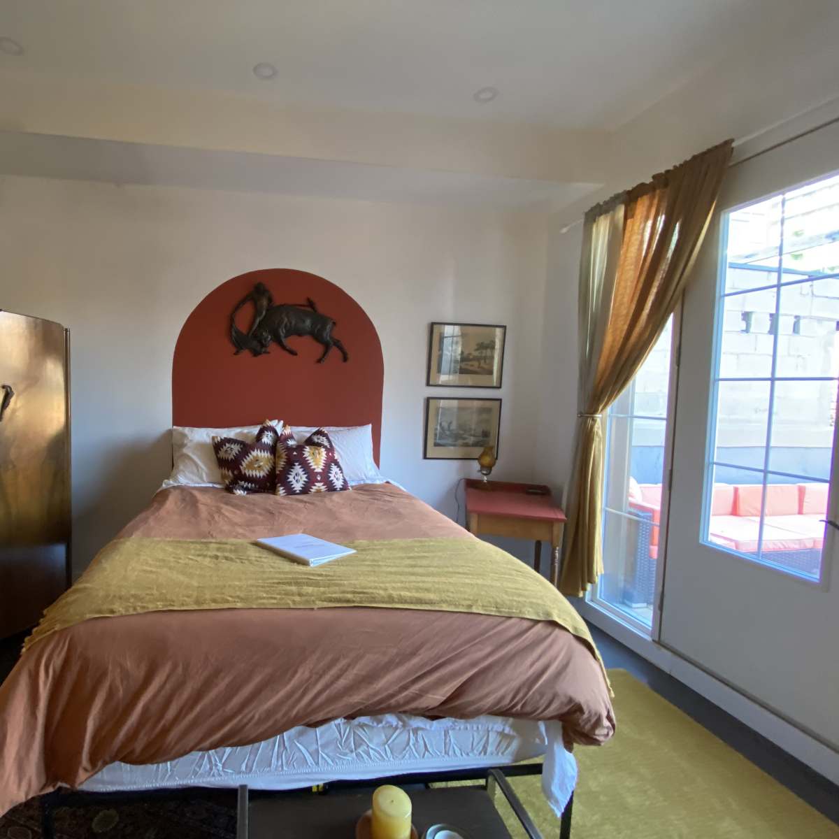 A cozy bedroom featuring a bed with an orange-brown cover, a wooden wardrobe, and a small table by a window.