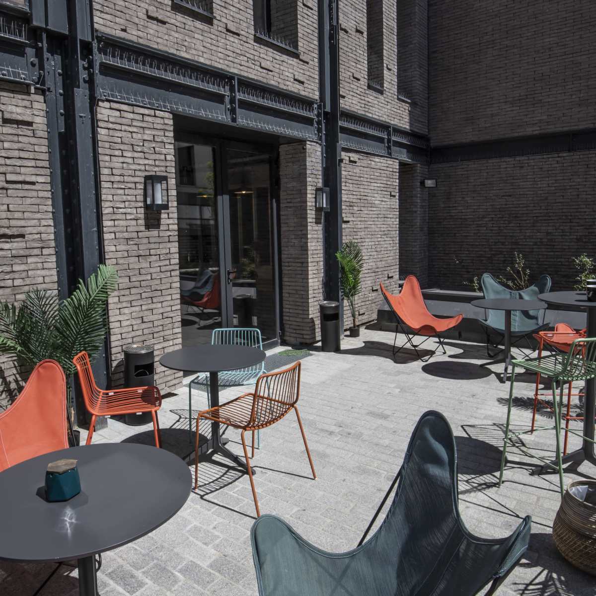 A modern outdoor seating area with various chairs and tables surrounded by brick walls and potted plants.