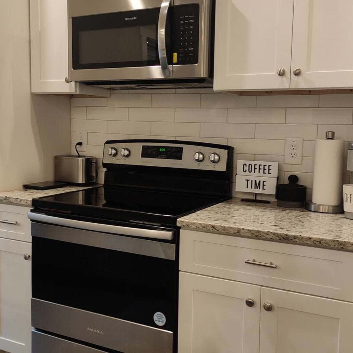 A kitchen with a stainless steel stove and microwave, white cabinets, and a countertop with a coffee-themed decoration.