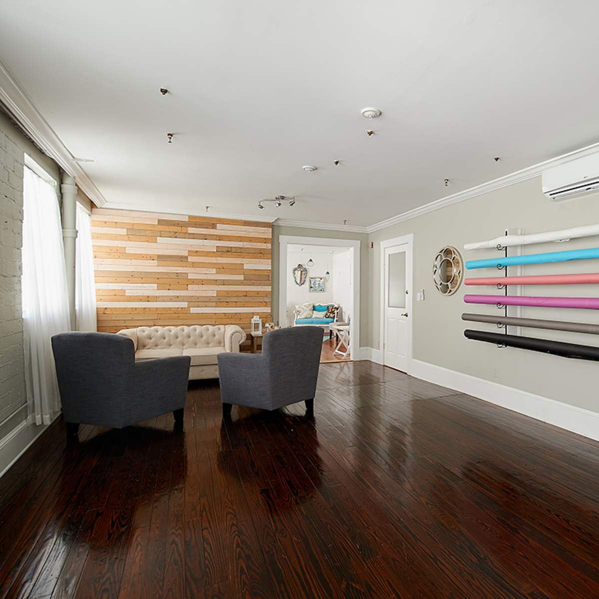 A spacious room with a wooden accent wall, two gray armchairs, and a wall-mounted display of colorful exercise bands.