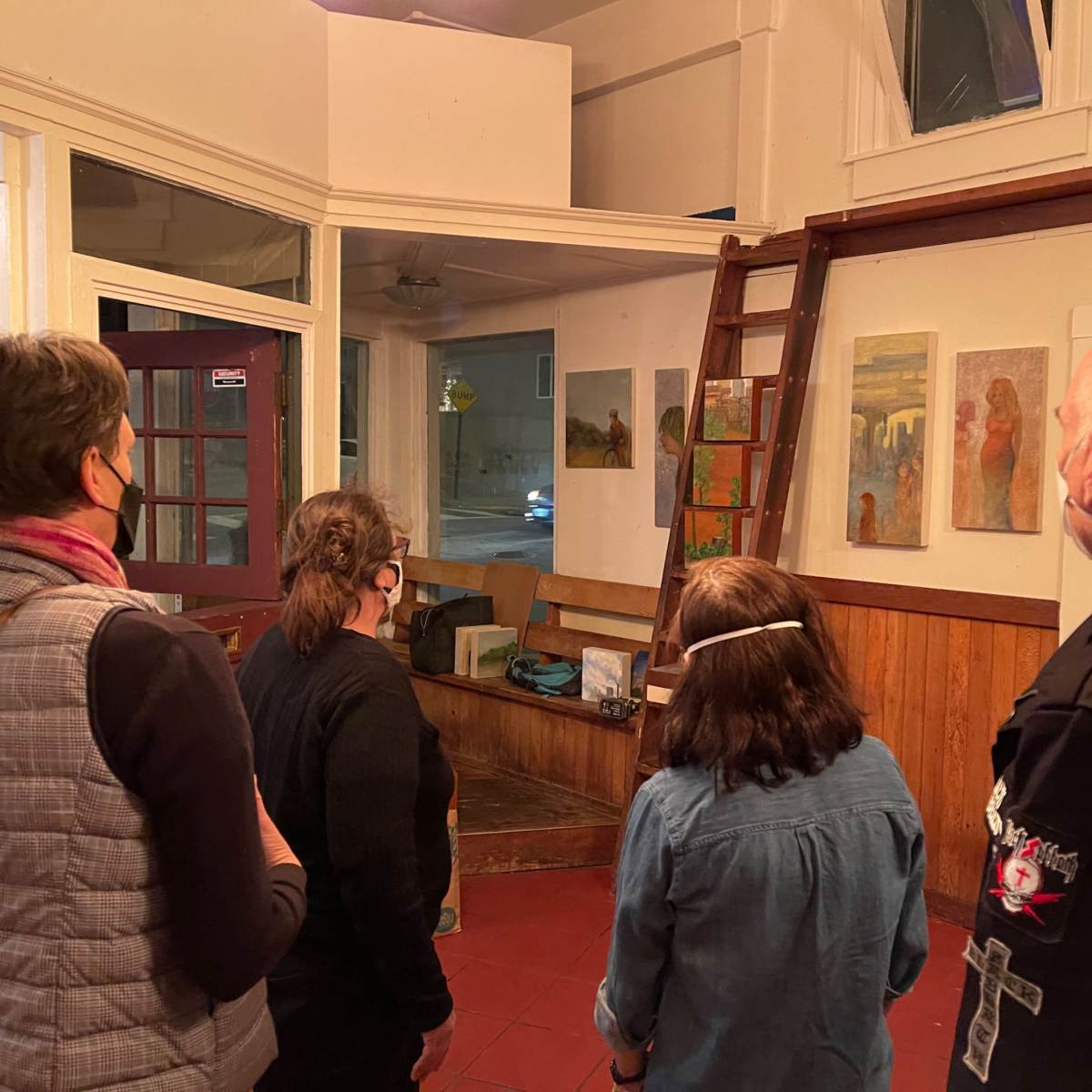 Four people observe artwork displayed on walls in a gallery setting.