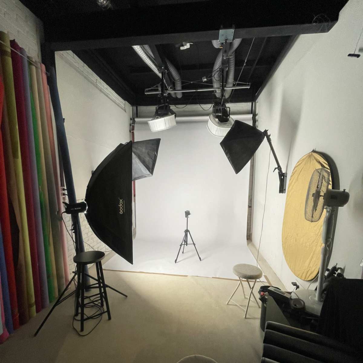 A photography studio equipped with lighting equipment, backdrops, and a central tripod on a light-colored floor.