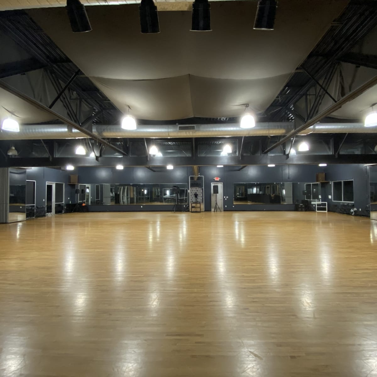 An empty dance studio with wooden floors, large mirrors, and overhead lighting fixtures.