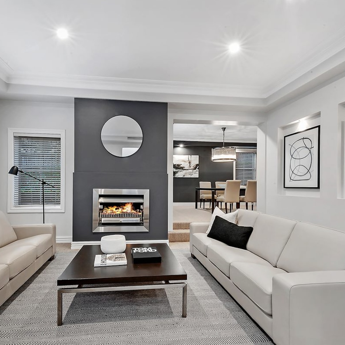 The living room features two light-colored sofas facing a central coffee table, with a fireplace and a circular mirror on the wall in the background.