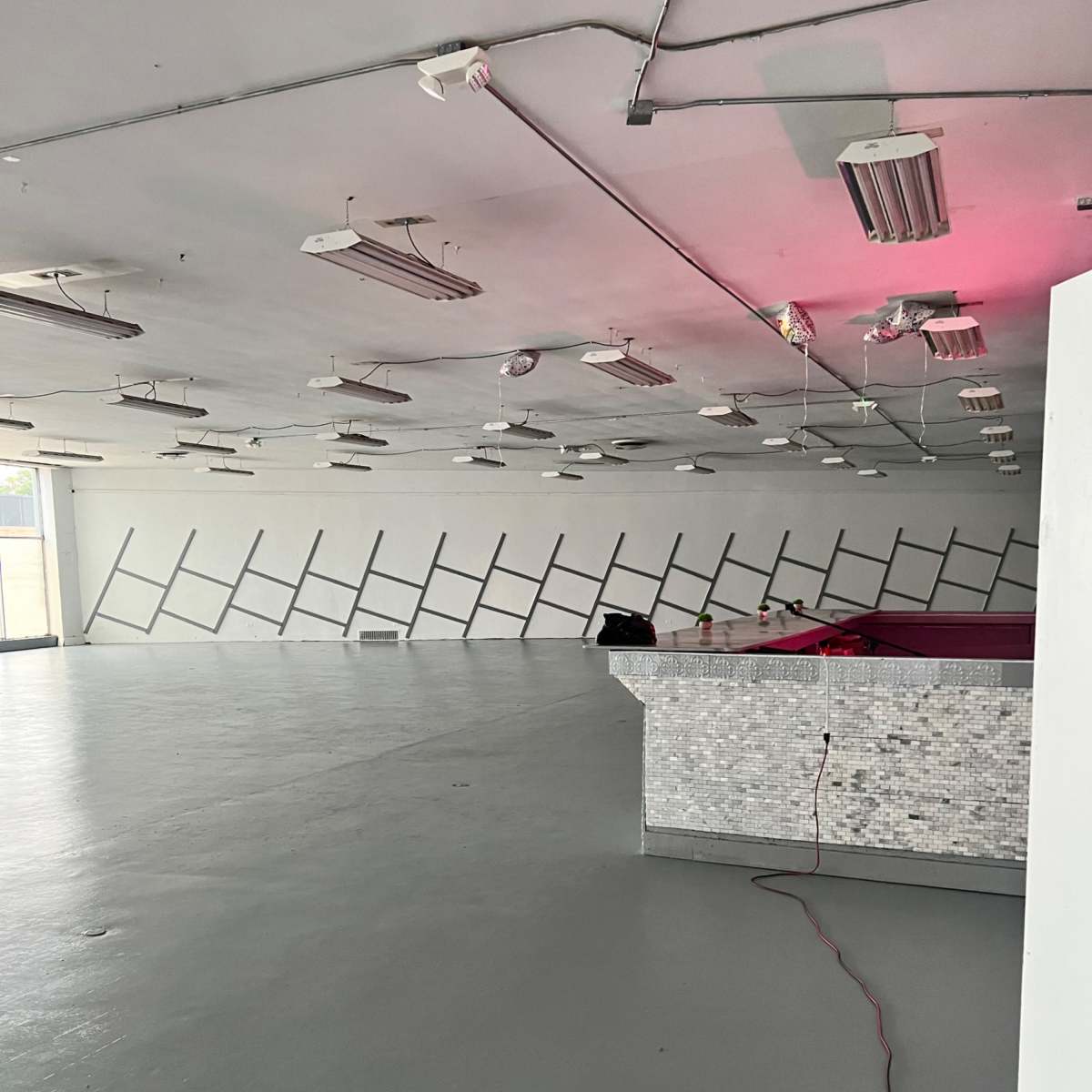 A spacious, empty room with a gray floor and a mirrored bar counter, featuring a diagonal pattern on the walls.