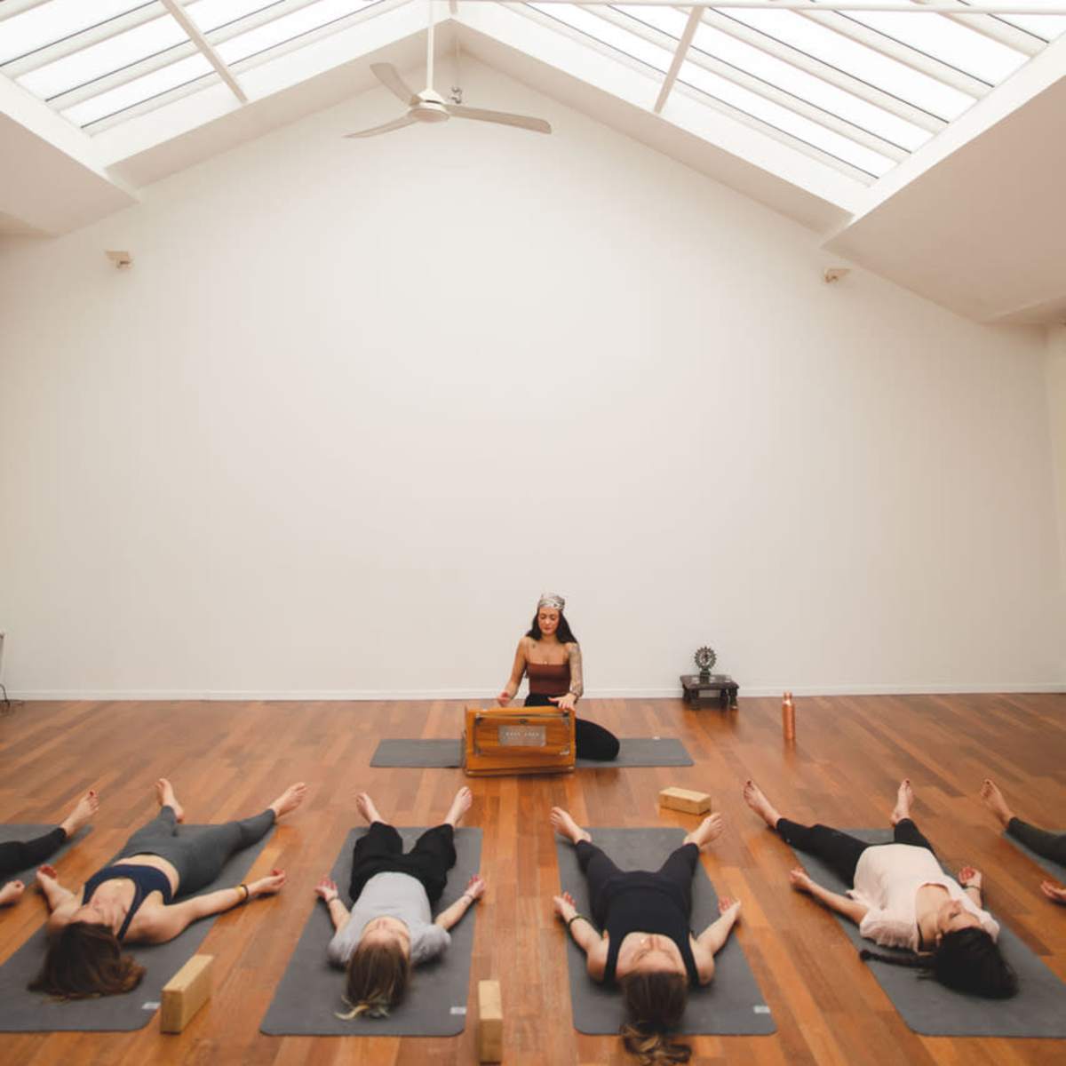 A group of people are practicing yoga in a bright, spacious studio, with a teacher positioned at the front.