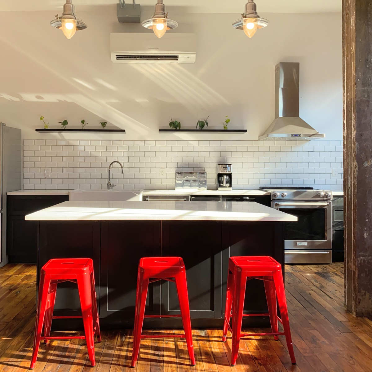 A modern kitchen features a central island with three red stools, stainless steel appliances, and white subway tile backsplash.
