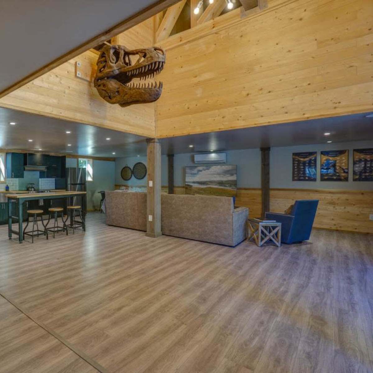 A spacious interior with wooden walls, a staircase leading to an upper level, and a living area featuring a sofa, a blue chair, and a kitchen in the background.