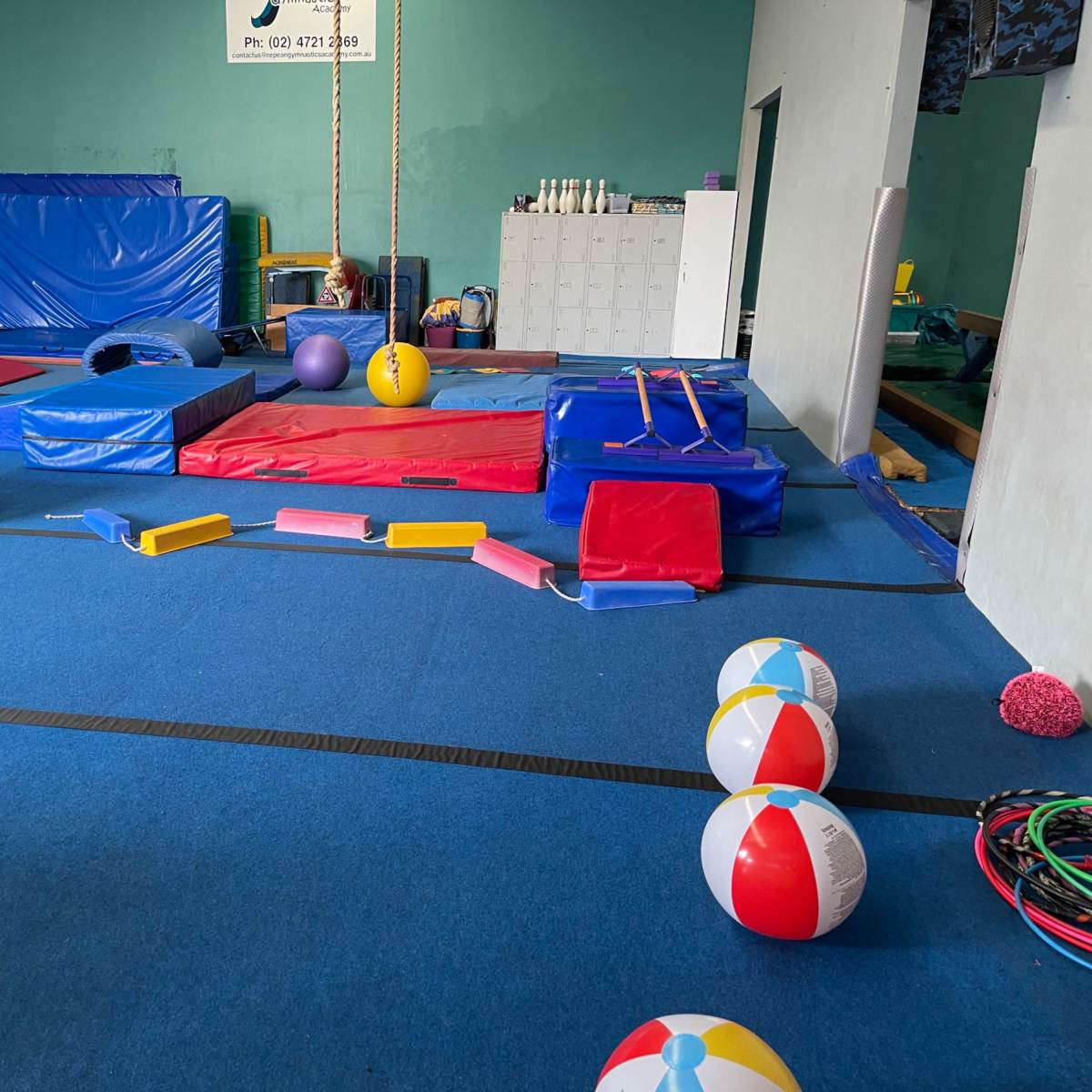 A brightly colored gymnastics or play area filled with various mats, equipment, and exercise balls arranged on a blue rubber floor.