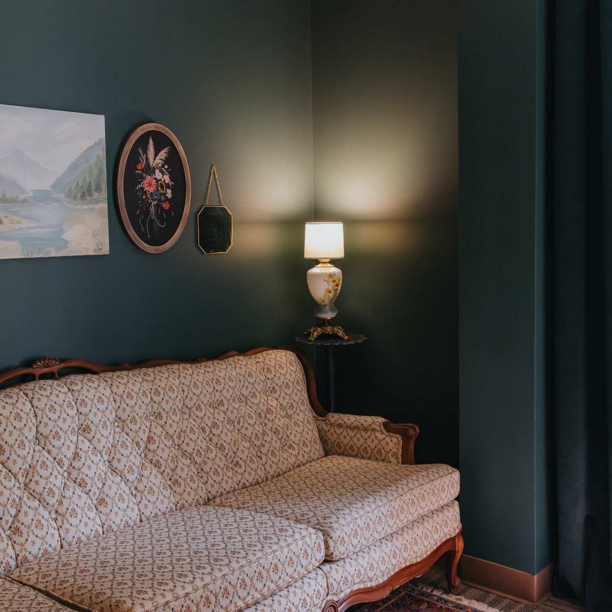 A living room with a patterned sofa, a painting of a landscape on the wall, and a lamp on a side table.