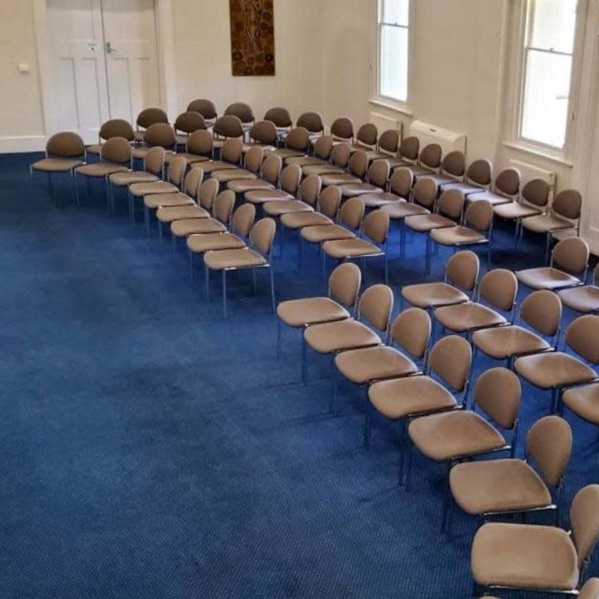 A meeting room with rows of empty, beige chairs set up on a blue carpet.