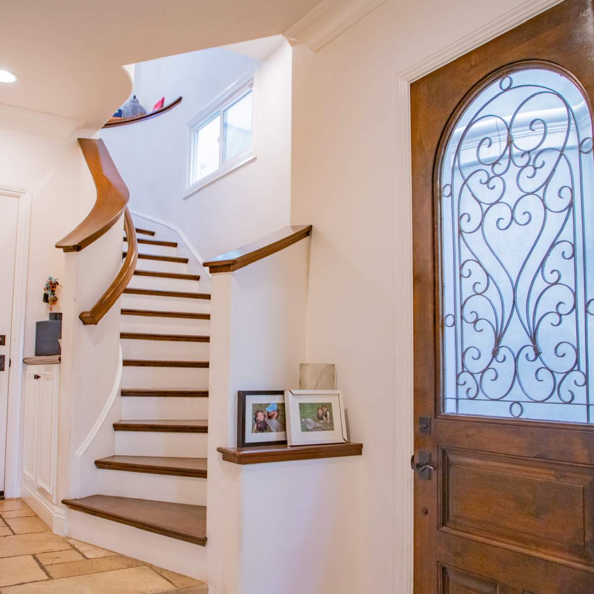 A foyer with a wooden front door, decorative wrought iron details, and a staircase leading to an upper level.