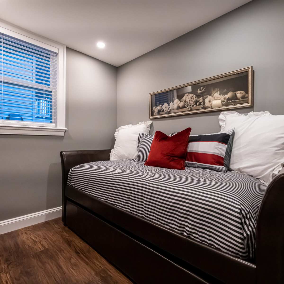 A small bedroom featuring a daybed with striped bedding and decorative pillows, positioned against a gray wall near a window.