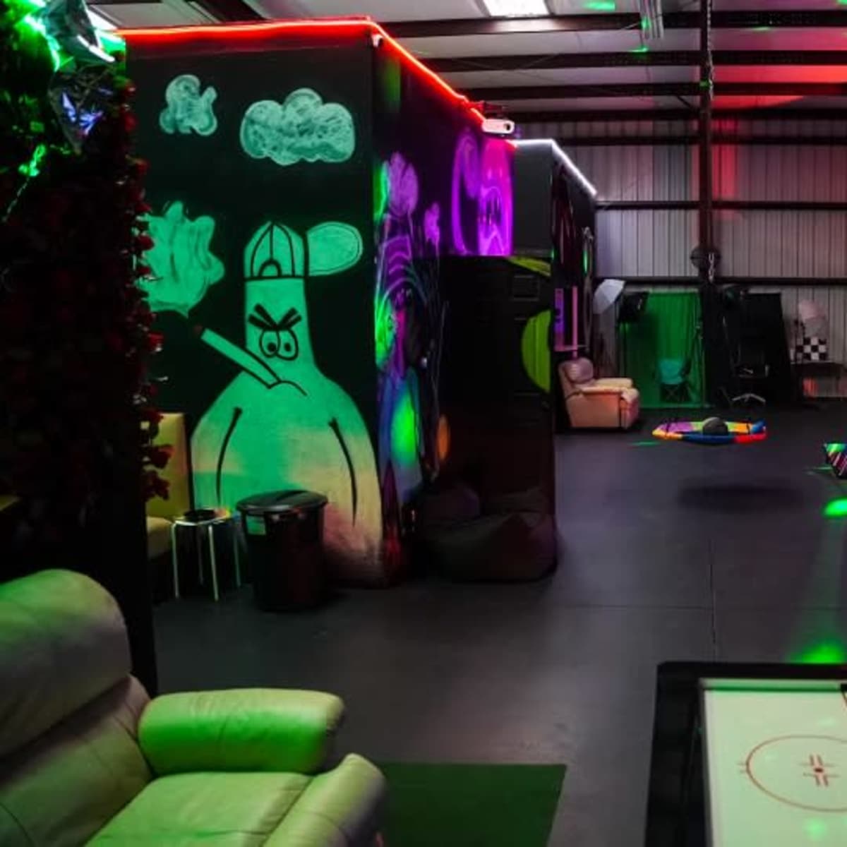 An indoor recreational space featuring colorful lighting, a mural on one wall, and various play areas with a foosball table and seating arrangements.