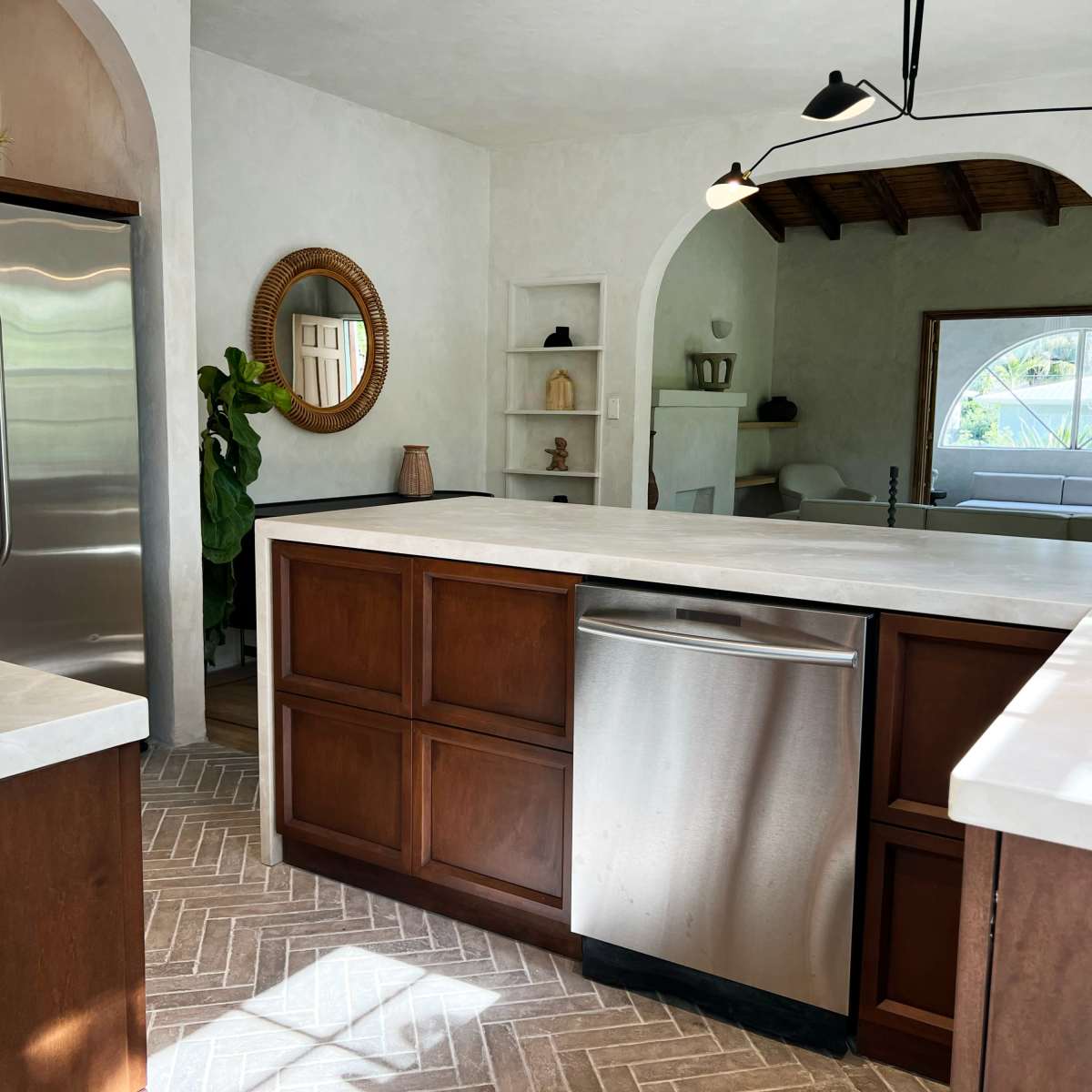 A modern kitchen featuring a large island with a stainless steel sink and dishwasher, surrounded by wooden cabinetry and a stainless steel refrigerator.