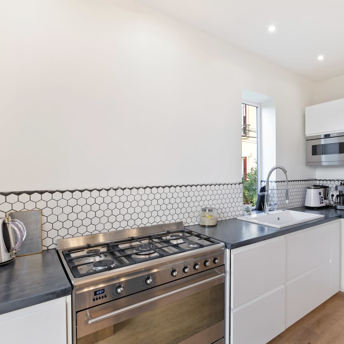 A modern kitchen features a gas stove, a sink, and built-in appliances with white cabinetry and hexagonal tile backsplash.