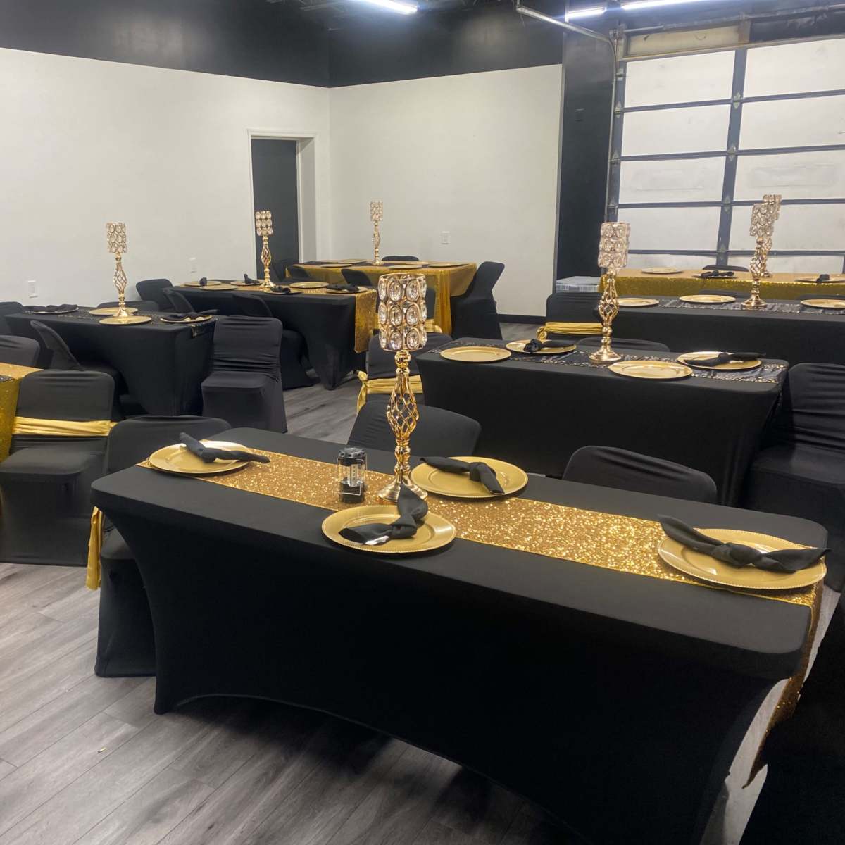 A spacious event room set up with multiple tables, each adorned with black table covers, gold accents, and elegant centerpieces.