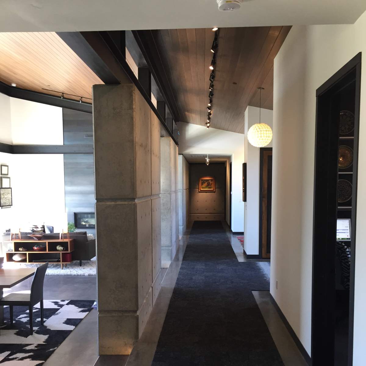 A modern hallway with concrete walls, a dark carpet, and a light fixture hanging from the ceiling, leading to a living area.