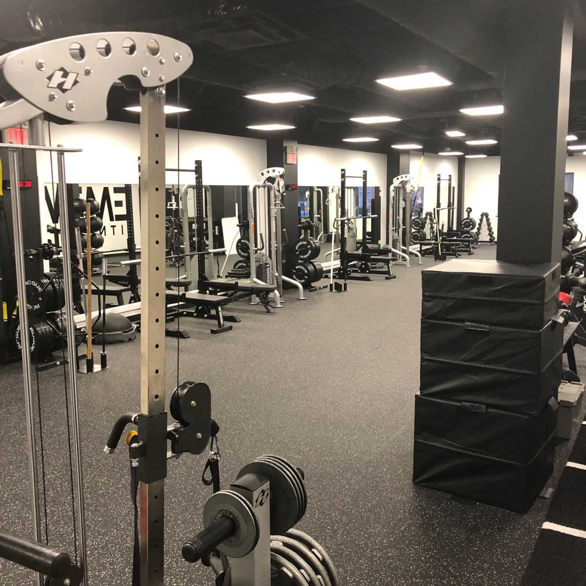 An indoor gym facility with various weightlifting equipment and a black rubberized floor.