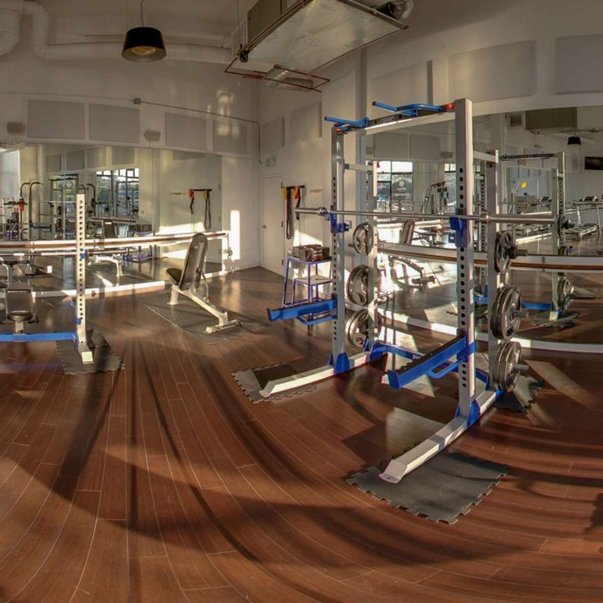 A spacious gym interior with various weightlifting equipment and large mirrors against the walls.