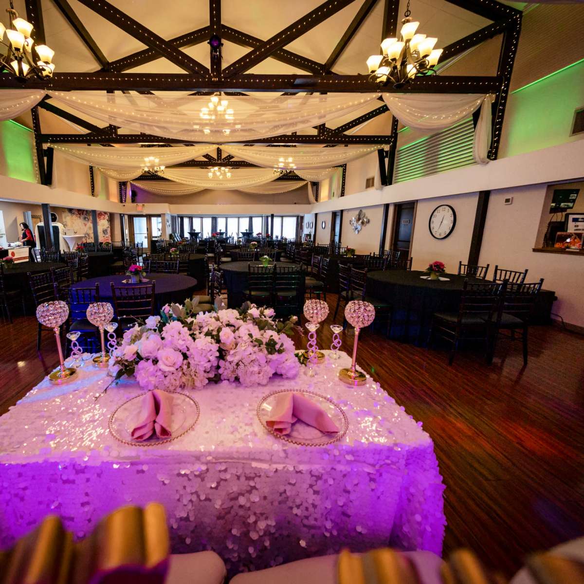 A spacious banquet hall with tables set for a wedding reception, featuring a decorated head table adorned with floral arrangements and elegant centerpieces.