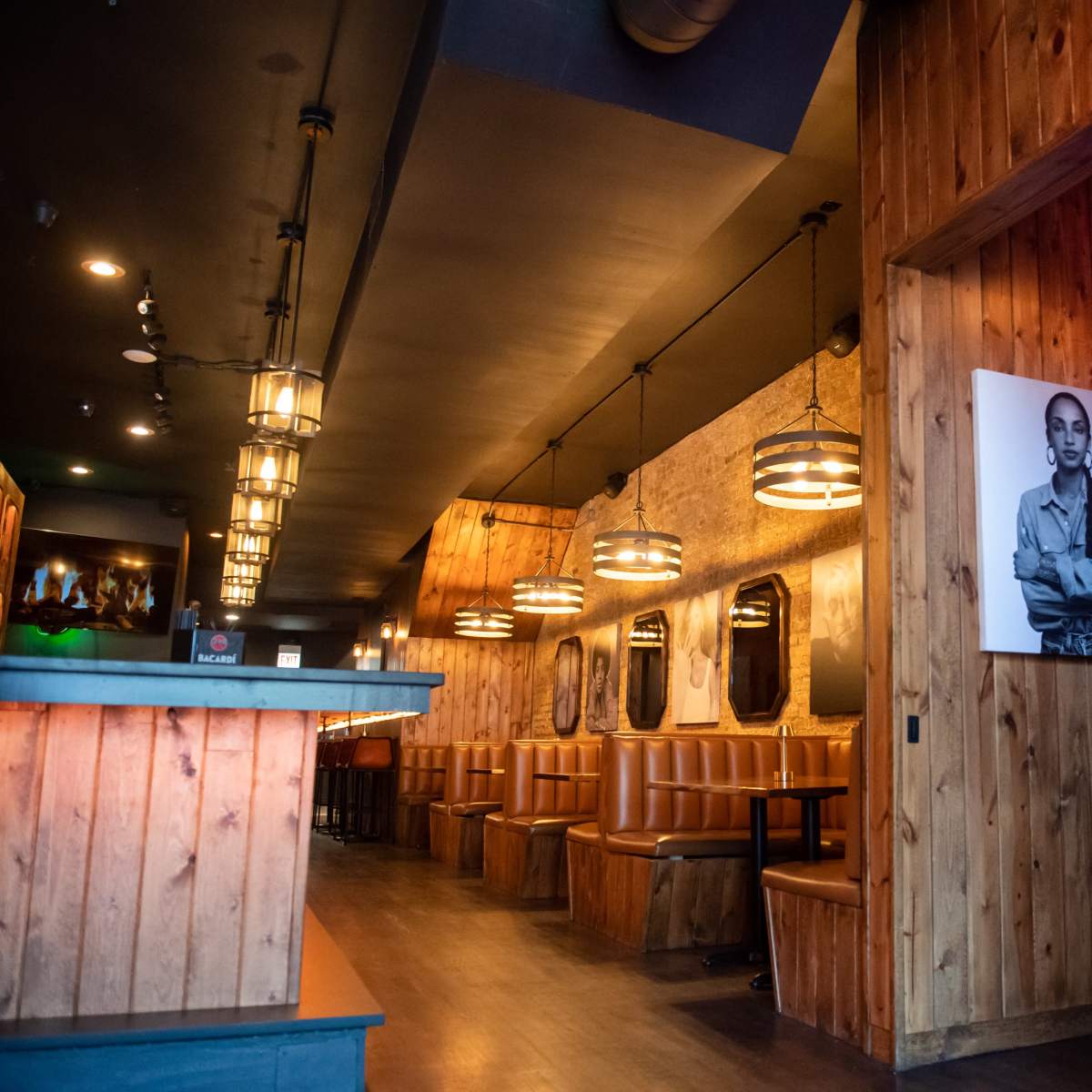 The interior of a restaurant with wooden paneling, booths along the walls, pendant lights hanging from the ceiling, and a neon sign that reads "Save Water Drink Champagne."