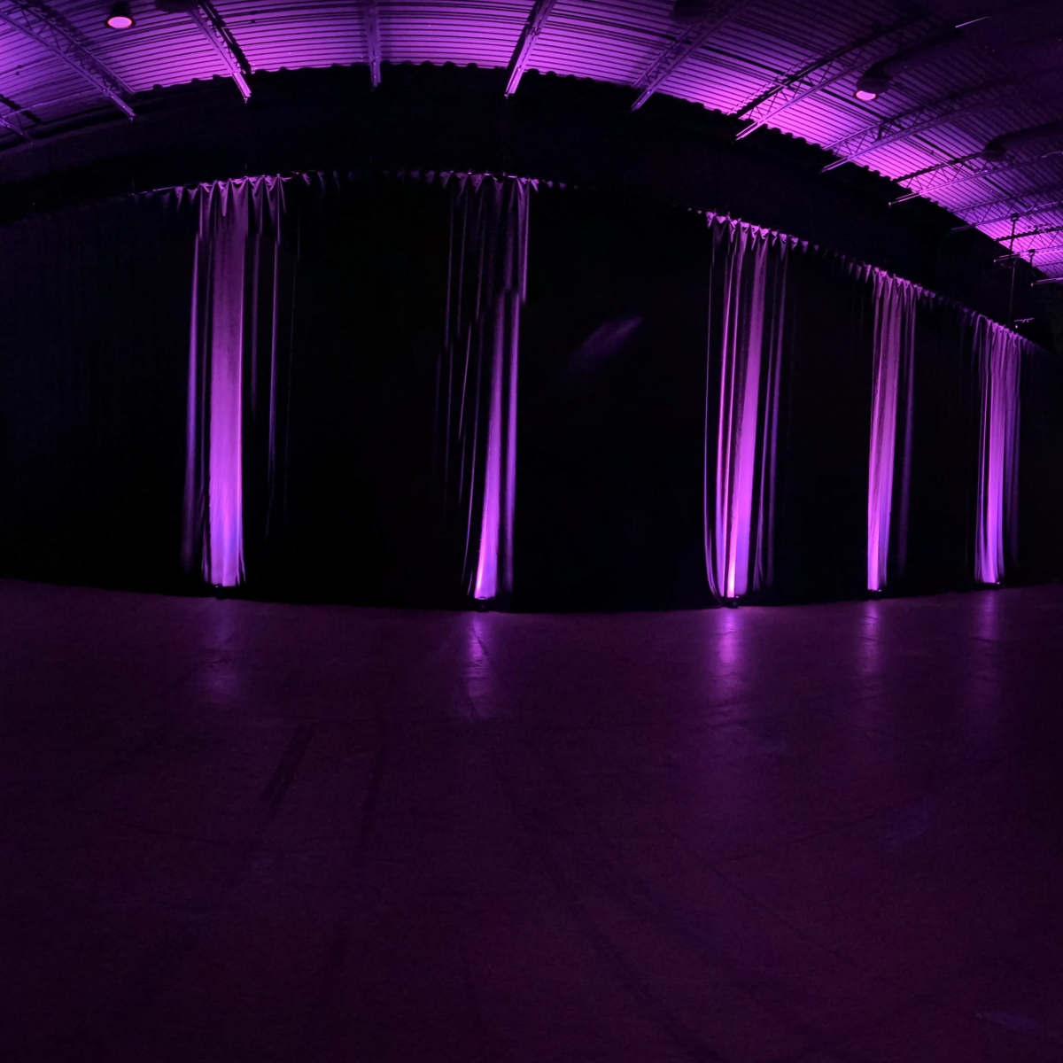 A dimly lit interior space with purple lighting illuminating dark curtains along the walls.