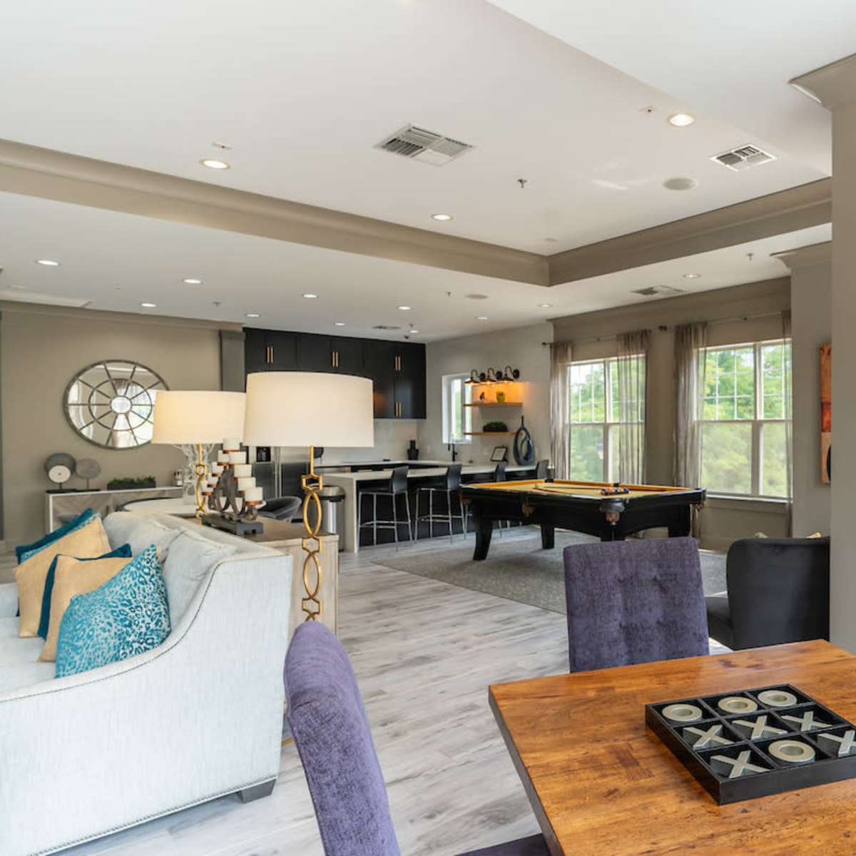 A modern living area featuring a dining table with chairs, a pool table, and an open kitchen area with large windows.