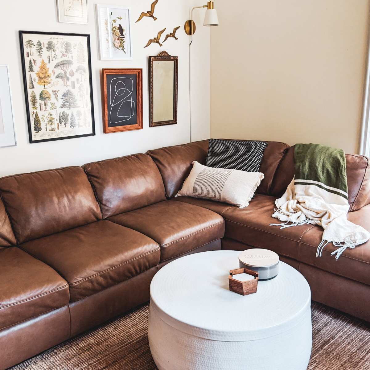 A brown leather sectional sofa positioned against a wall adorned with framed artwork, alongside a round white coffee table and various decorative items.