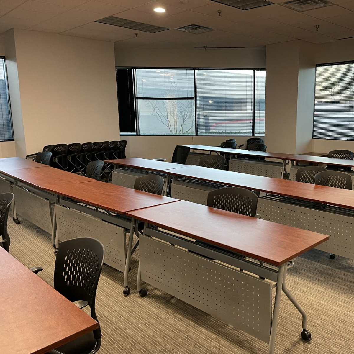 A classroom with rows of tables and chairs arranged near large windows.