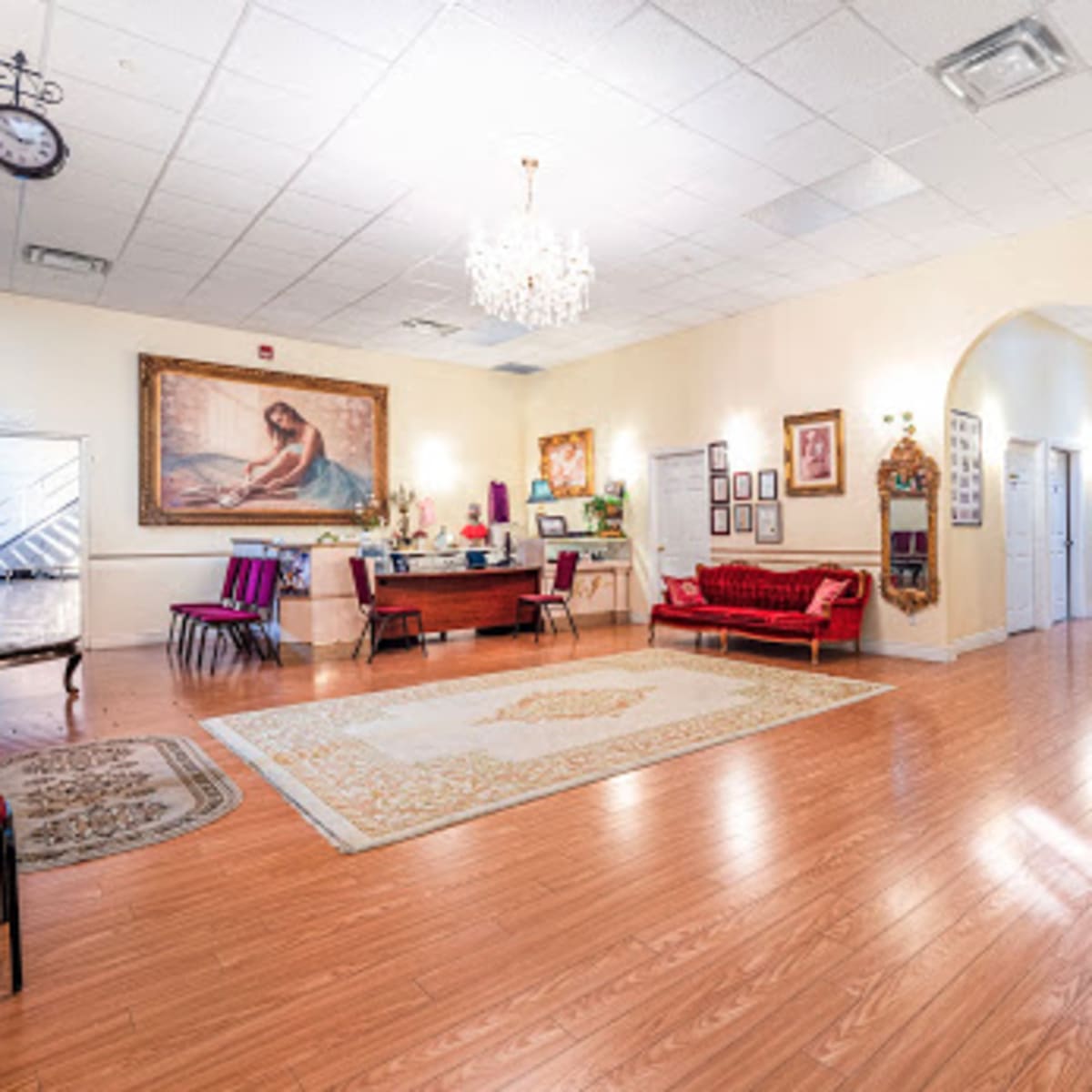 A spacious reception area with hardwood floors, a large ornate painting on the wall, a chandelier, and a mix of seating arrangements.