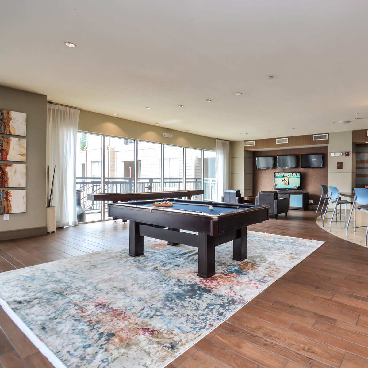 A spacious recreation area featuring a pool table, seating, and a bar along with large windows allowing natural light.