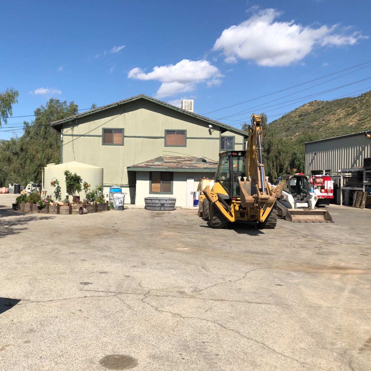 A construction site features a large green building surrounded by heavy machinery and a clear blue sky.