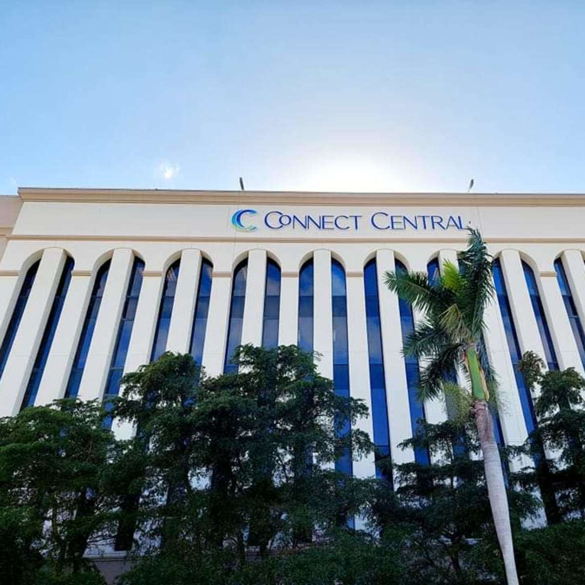 A building with the name "Connect Central" prominently displayed on its facade, surrounded by palm trees and sunlight.