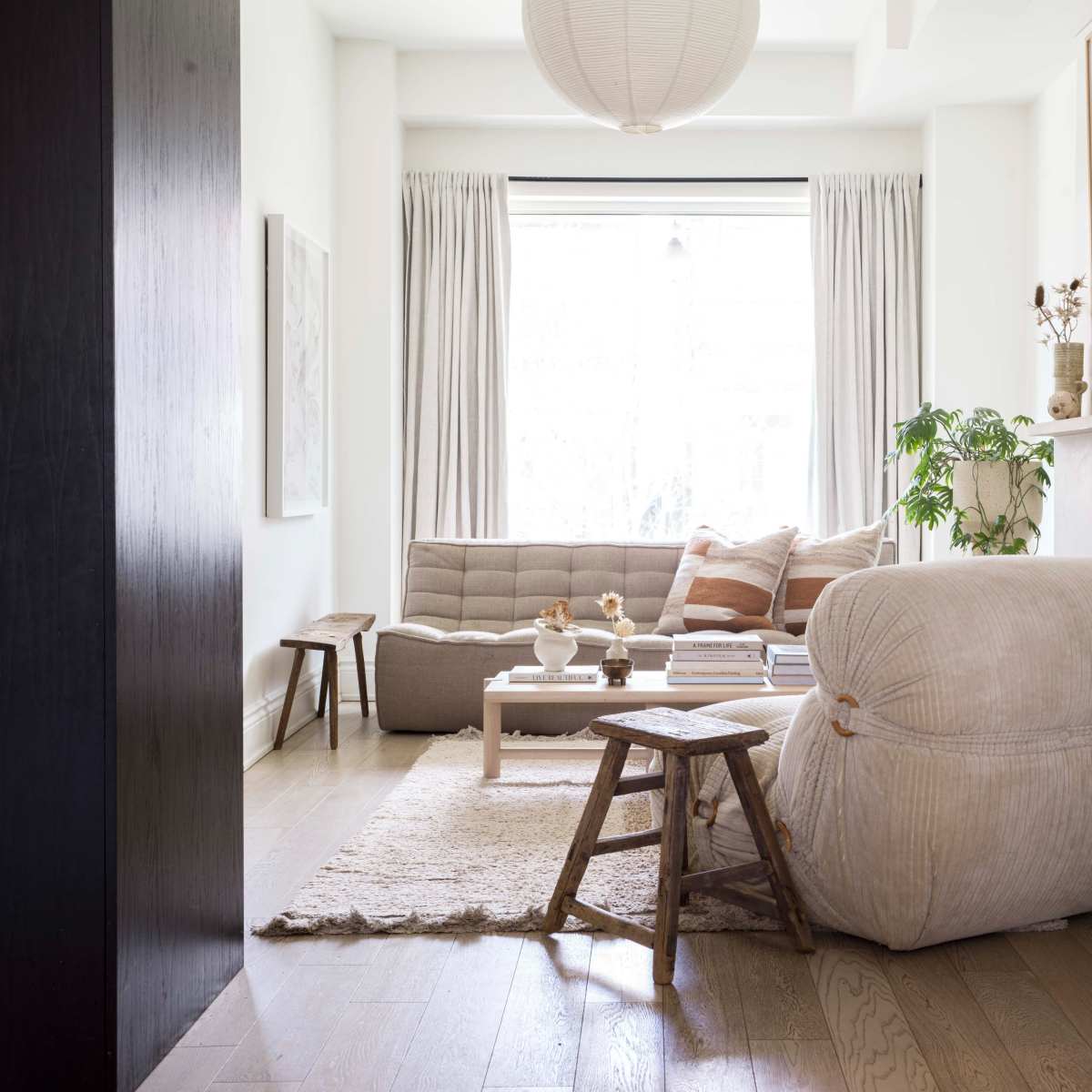 A light-colored living room with a sofa, a round coffee table, and a large floor cushion, all arranged around a soft rug under natural light from a window.