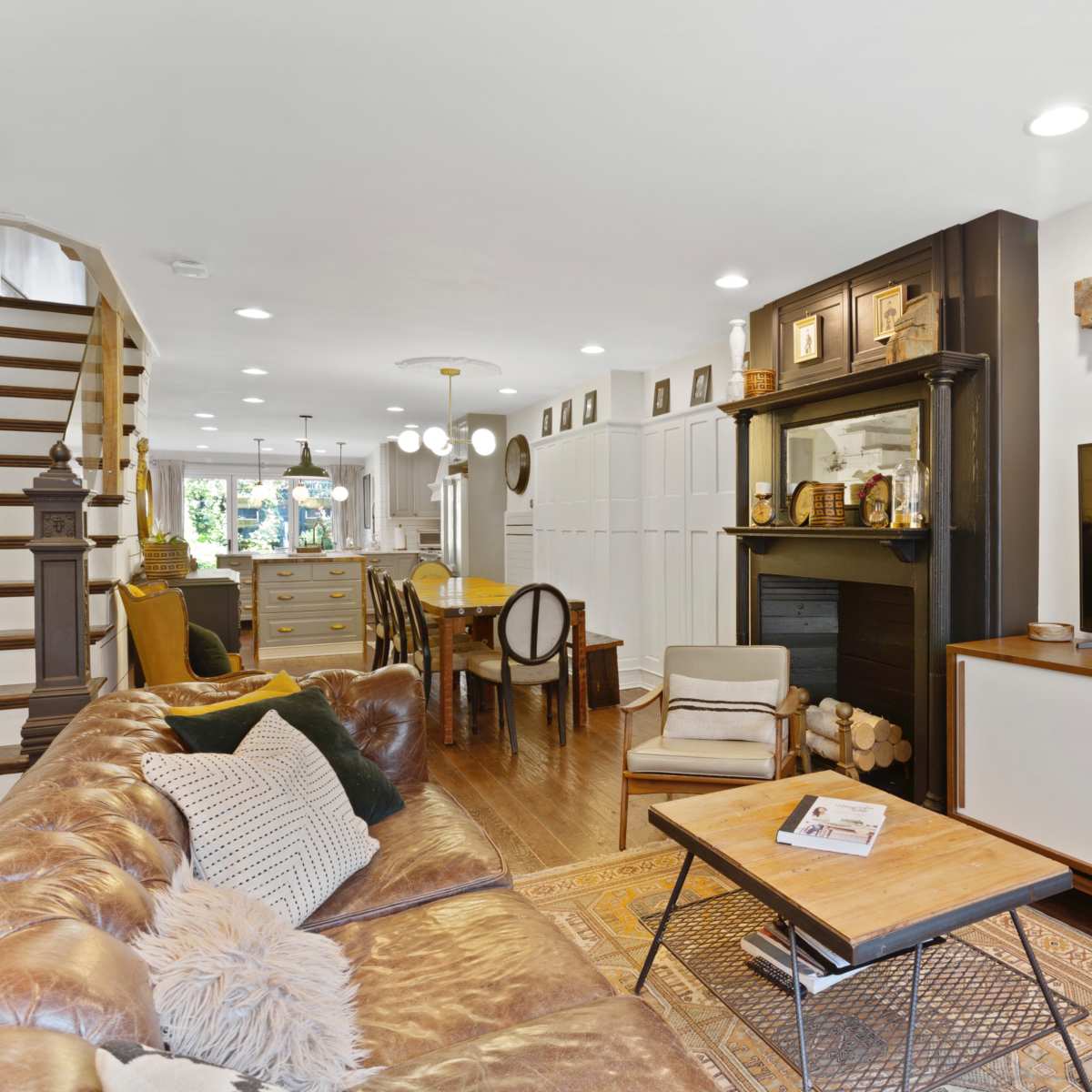 A modern living room featuring a leather sofa, a wooden coffee table, built-in shelving, and a staircase leading to an upper level.