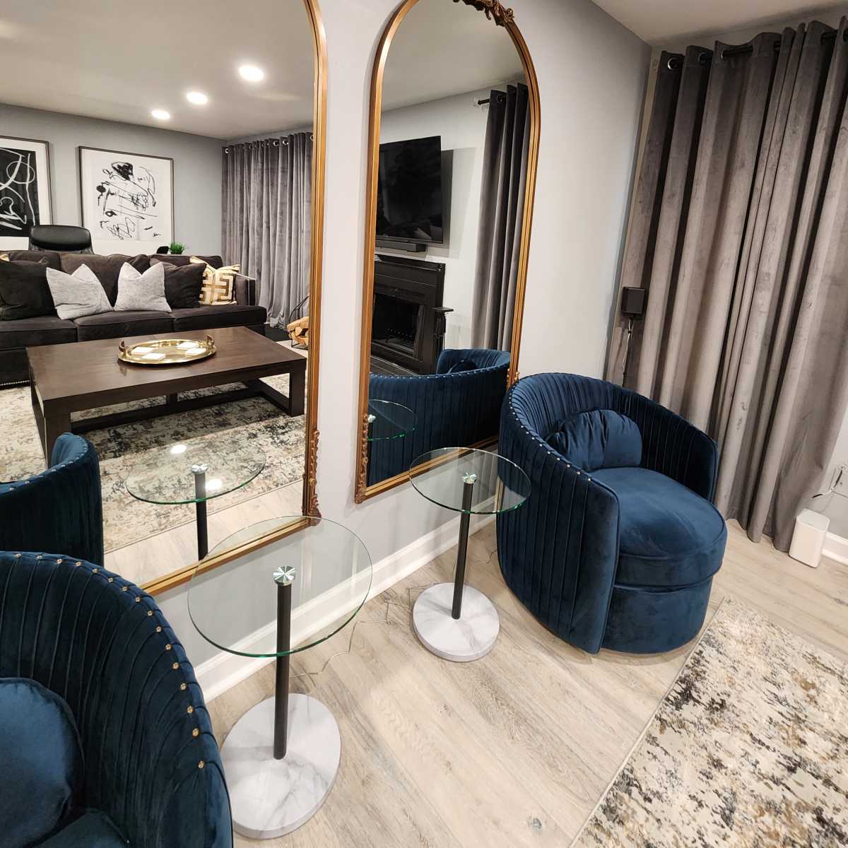 A living room with two ornate mirrors, a dark coffee table, and two blue armchairs beside glass side tables.