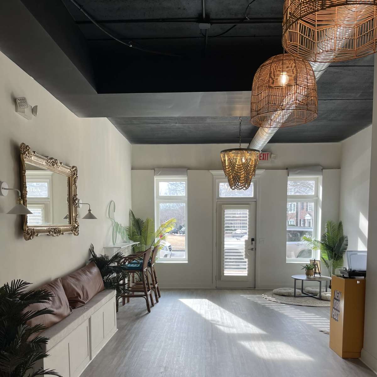 A bright, minimalist interior space featuring a brown leather bench, potted plants, and decorative pendant lights.