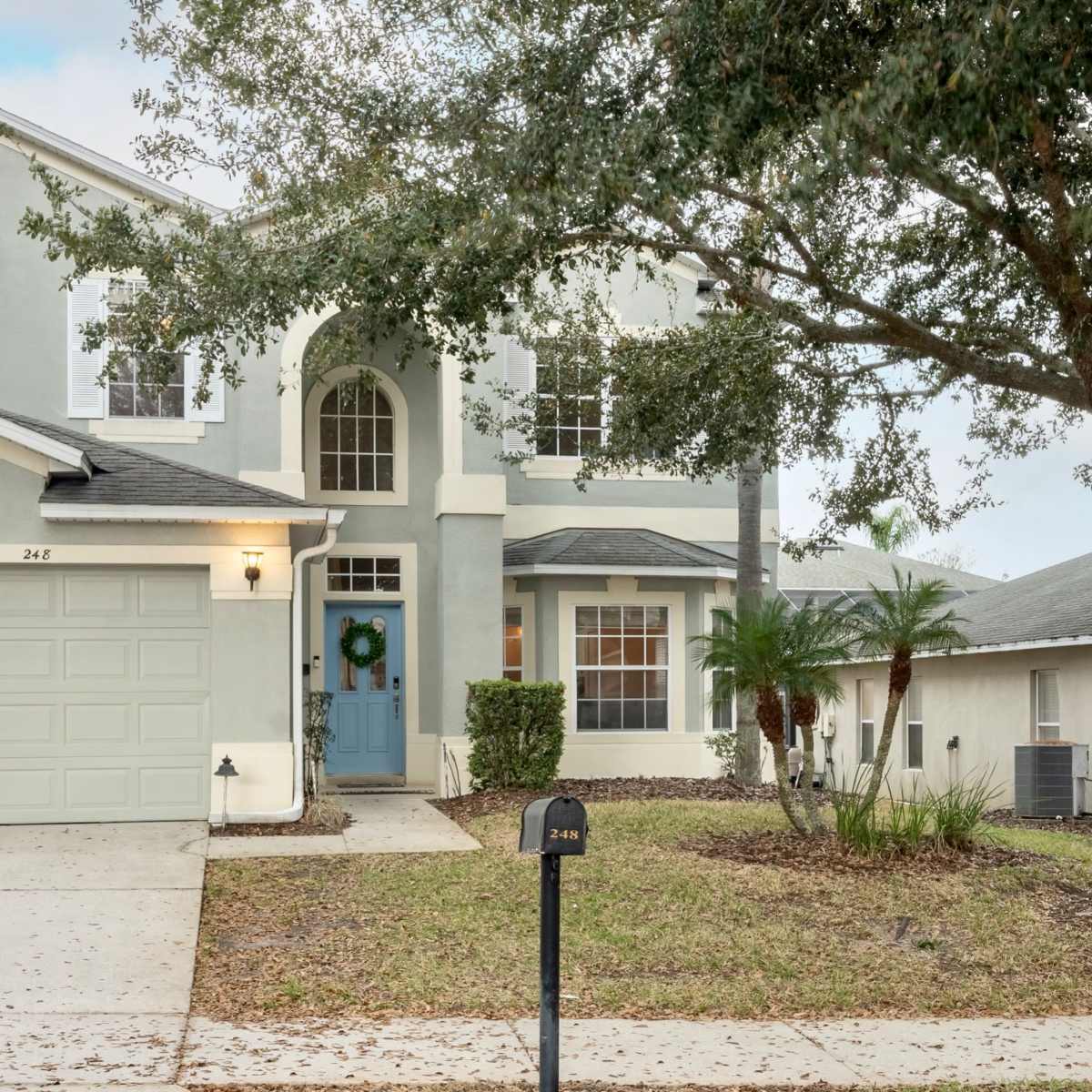 A two-story, light blue house with a two-car garage and a well-maintained front lawn.