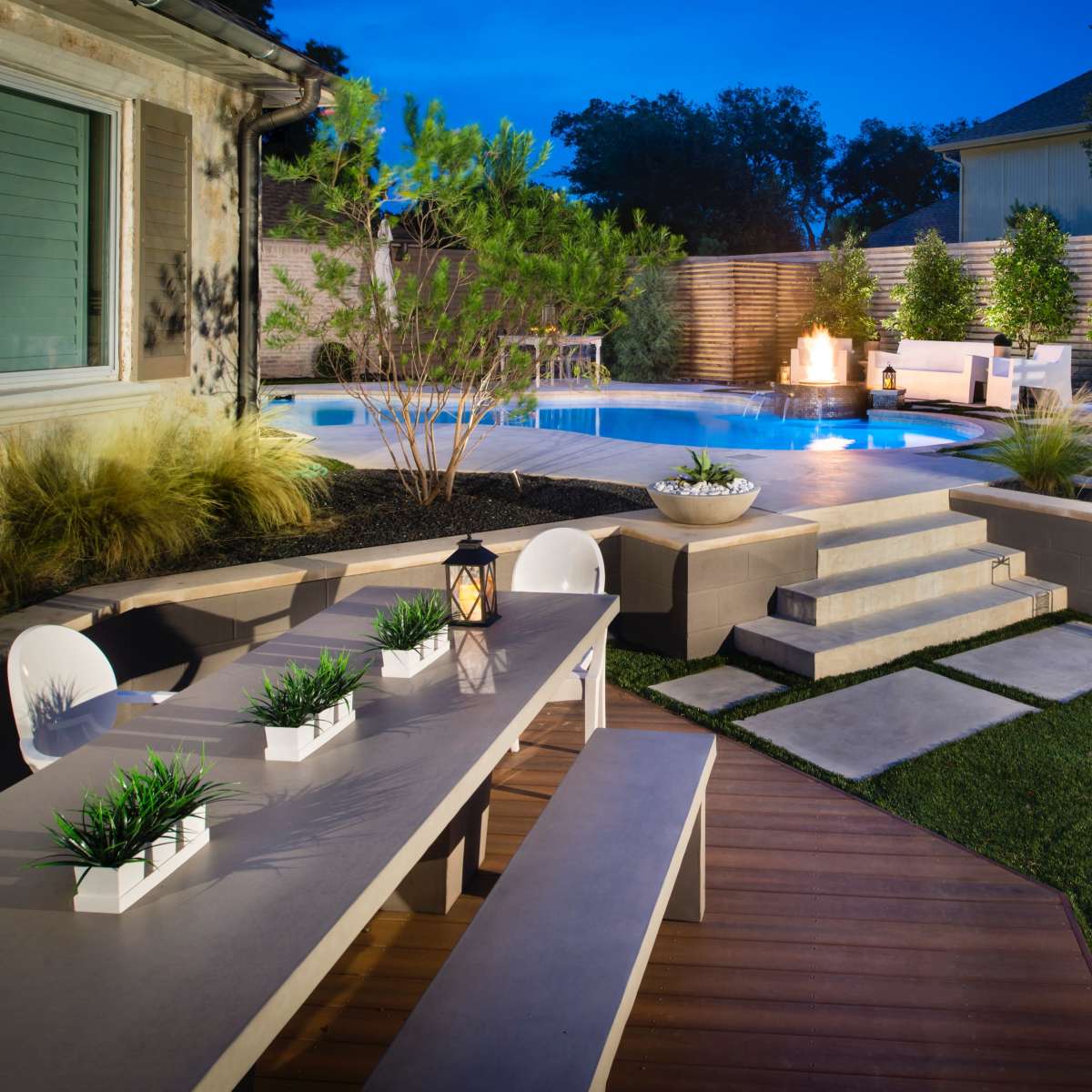 A modern backyard featuring a swimming pool, elegant seating areas, and a dining table under soft lighting.