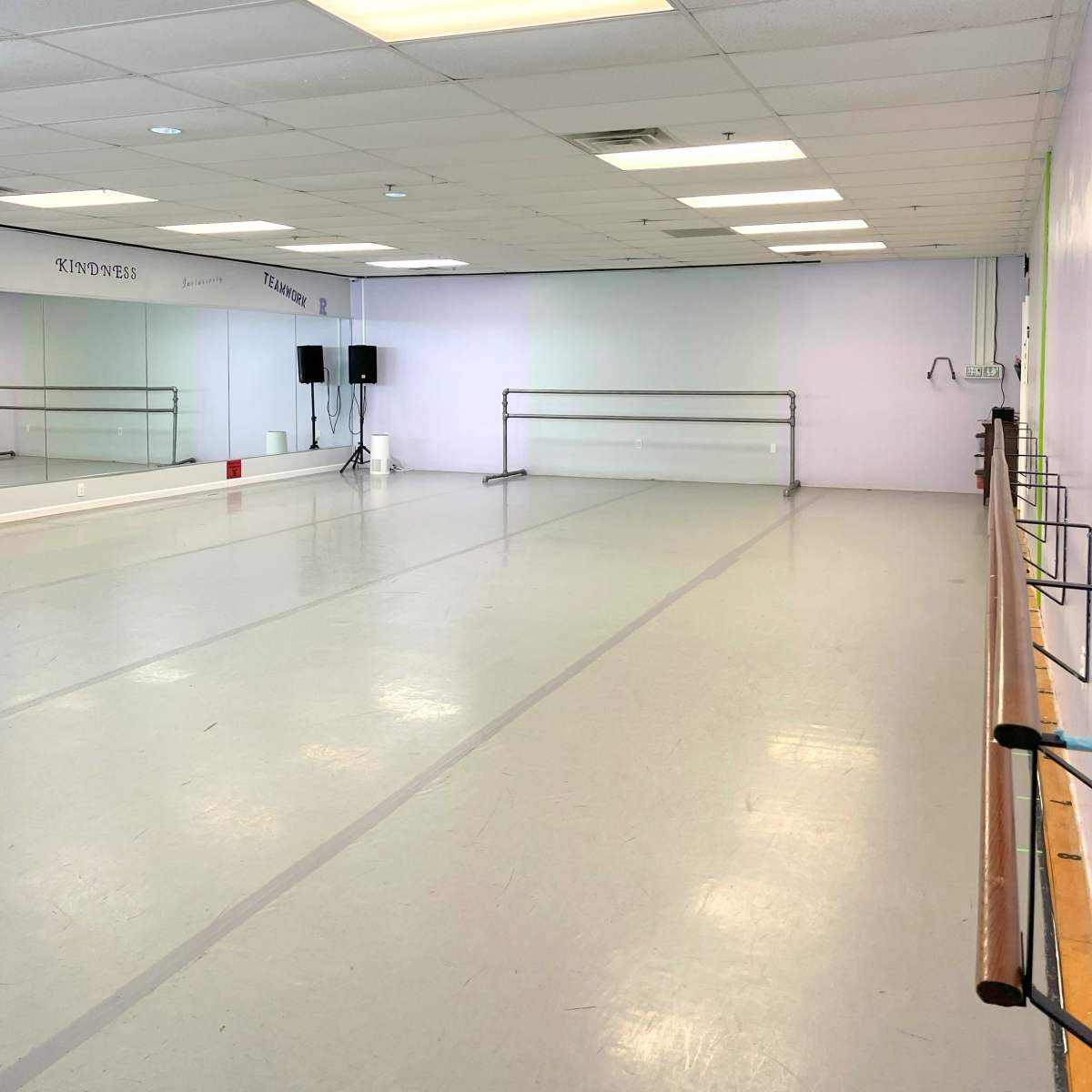 A spacious dance studio with mirrored walls, a wooden barre, and bright overhead lighting.