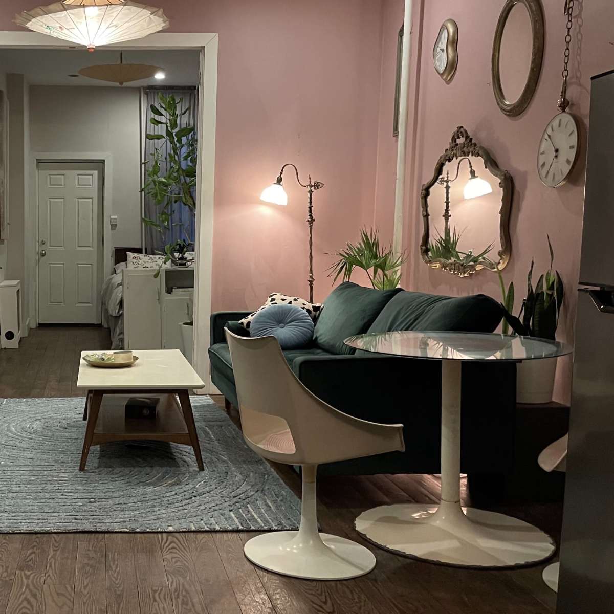 A cozy living space featuring a pink wall, a television, a green sofa, a round table with chairs, and decorative plants.