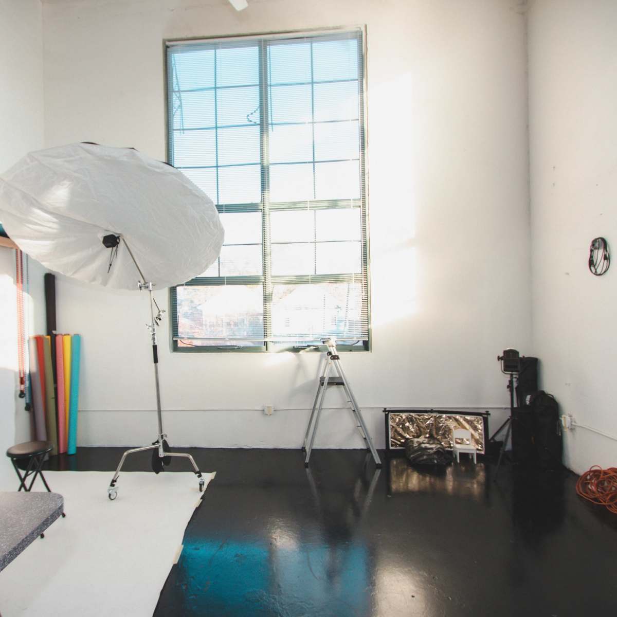 A photography studio with a large light umbrella, a tripod, colorful backdrops, and a black floor.