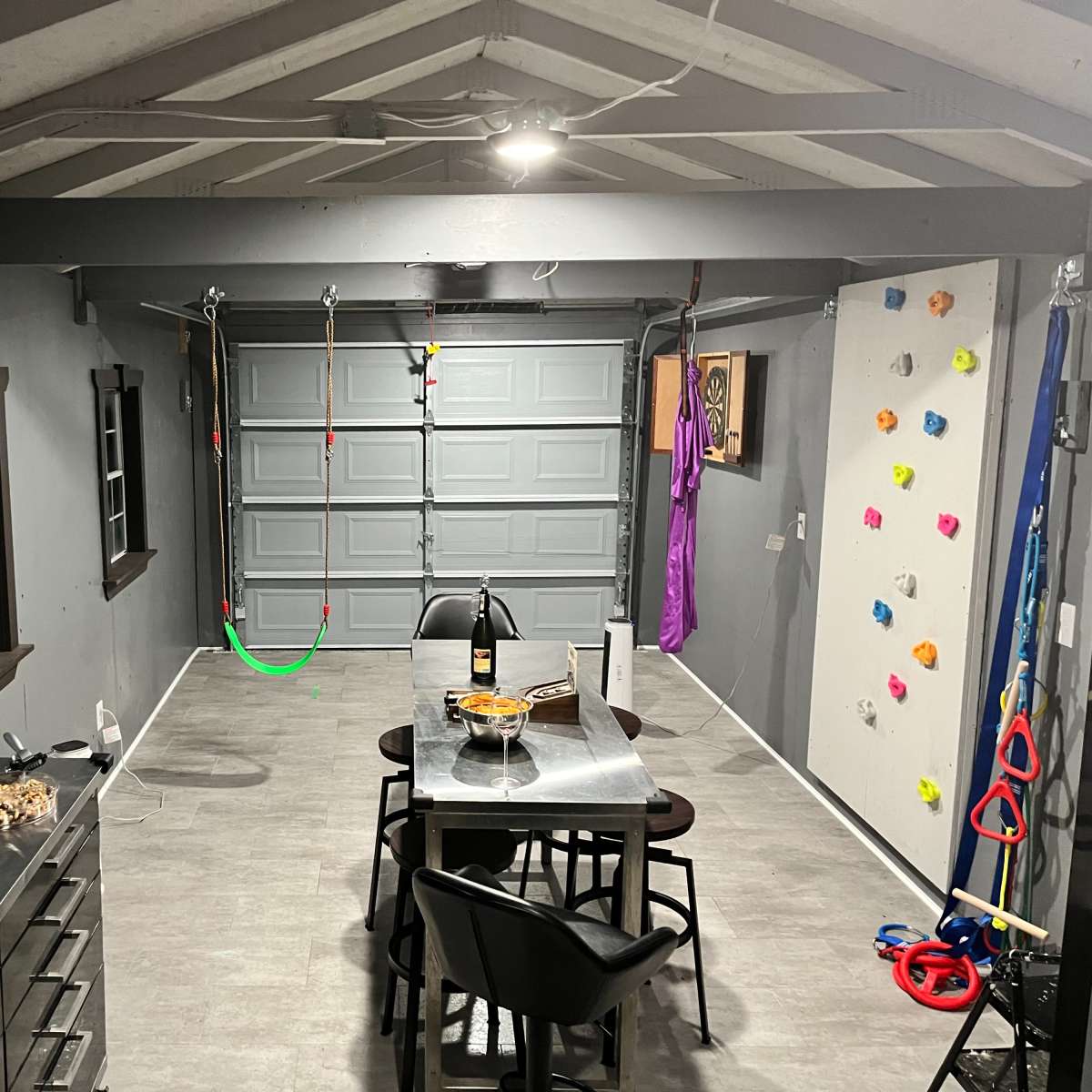 A garage converted into a multifunctional recreational space with a dining table, snack area, and climbing wall.