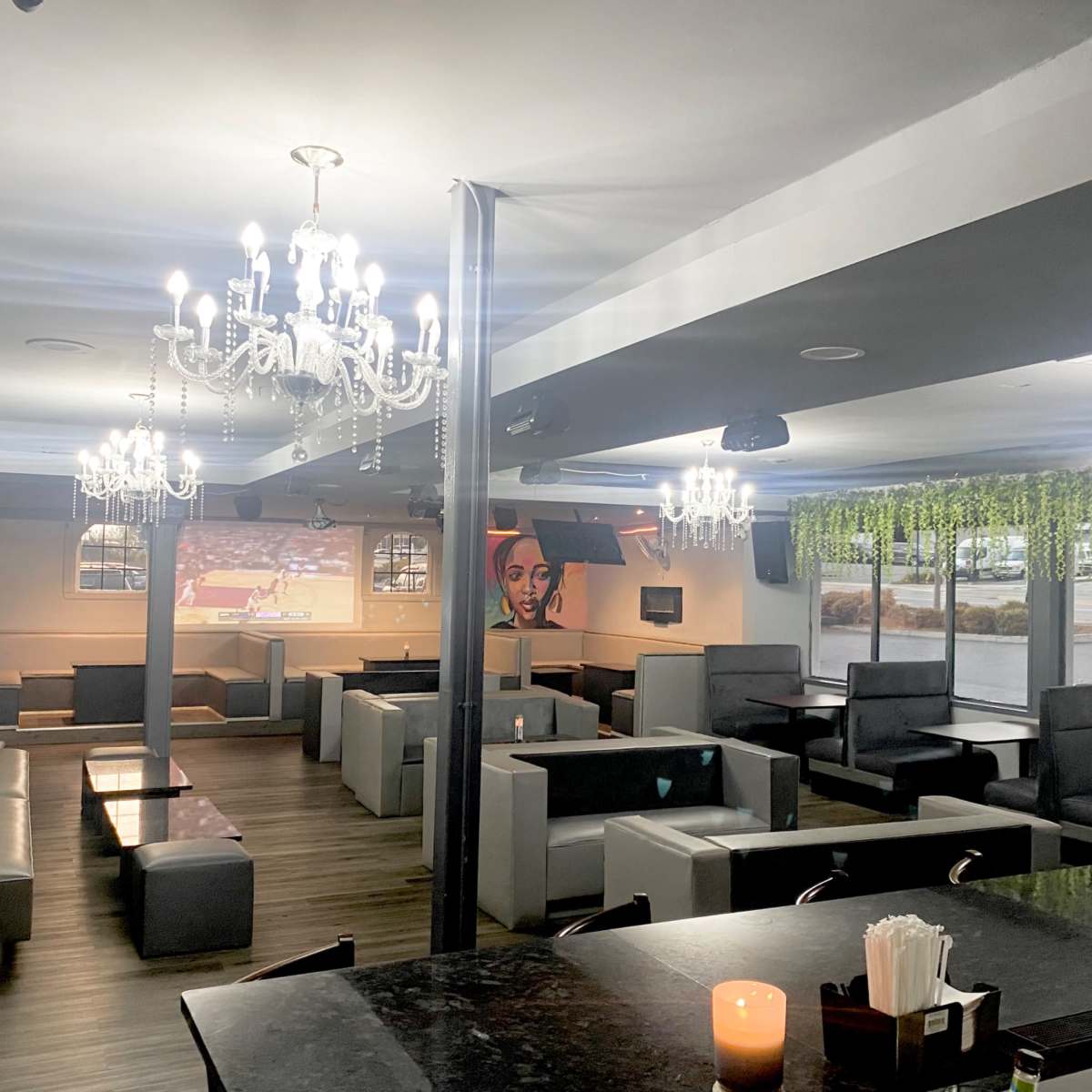 A modern restaurant interior featuring several booth seating areas, chandeliers, and greenery hanging from the ceiling.