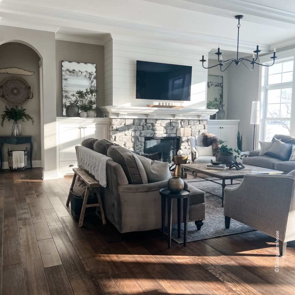 A well-furnished living room with a stone fireplace, a large TV mounted above it, and various seating arrangements around a central coffee table.