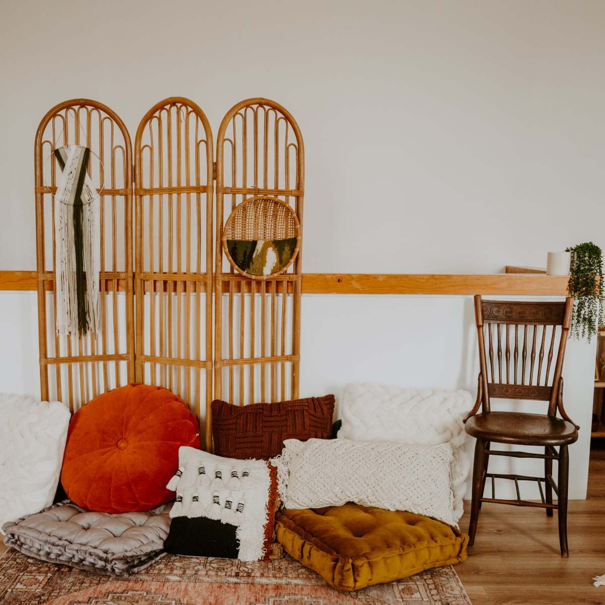 A cozy room with a wooden folding screen, assorted cushions on the floor, and a chair beside a bed.